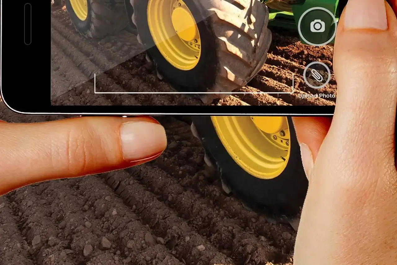 A phone held over a tractor tire in a field, photographing the damage for a Warranty Wizard claim