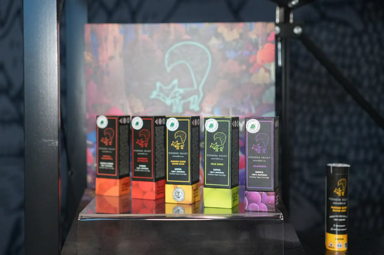 A lit retail shelf holding five Pioneer Valley vape cartons in their flavor colorways, with the fox illustration on the card behind them.
