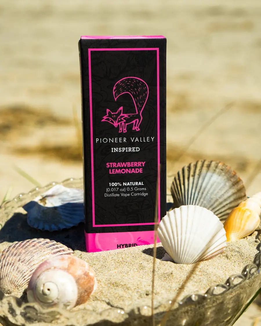 A Pioneer Valley Inspired Strawberry Lemonade vape cartridge carton standing in a dish of sand among scallop shells on a beach, portrait crop.