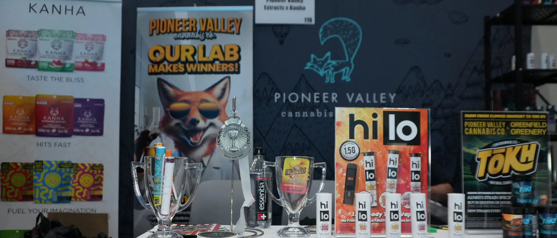The Pioneer Valley Extracts and Kanha trade-show booth: the Our Lab Makes Winners backdrop banner and Kanha pull-up beside the fox wall, with the full product table laid out in front.